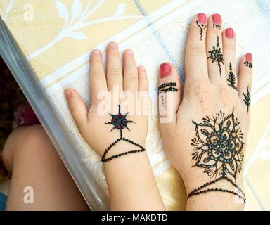 Hands of a mother and child with a traditional indian black flower tattoes on the table outdoors close-up Stock Photo