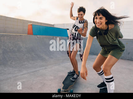 Young hipster girls riding on skateboards and having fun. Female friends together skateboarding at skate park. Stock Photo