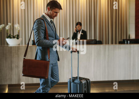 Young businessman walking in hotel lobby and using mobile phone. Business traveler arriving at his hotel. Stock Photo