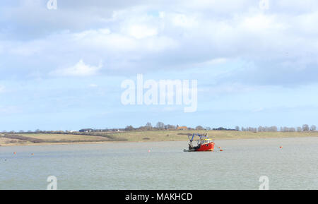 A fishing boat anchored in the Swale. The Isle of Sheppey in the background with the church of St Thomas the Apostle in the hamlet of Harty. Stock Photo