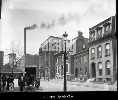 Horizontal, black and white photograph showing a row of two and three-story buildings from the opposite side of the street. There is a industrial building with a smokestack at the end of the street with a sign reading '(Polar Wa)ve Ice and Fuel Co.' Several African-American people are standing or walking down the sidewalk in the left foreground. Title: Lawton Street looking west to Beaumont. Polar Wave Ice and Fuel Company, Beaumont Medical College, and the home of Doctor Gustavus H. E. Baumgarten in the background.  . circa 1910. Holt, Charles Clement, 1866-1925 Stock Photo
