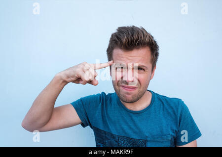 Young guy thinking about something, holding fingers on temple, trying to find a solution on blue background Stock Photo