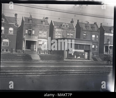 Horizontal, black and white photograph showing a row of two-story, single-family brick homes, probably on Delmar between Union and Kingshighway. The view is looking across the road and streetcar rails towards the house in the center, which has an attached storefront on the ground floor. A small poster with a light background and a cross in the center can be seen in many of the windows, possibly a Red Cross Service Flag given out during World War I. A partial view of a horse on the road can be seen to the right. A note on a print made from this negative reads 'Zoning', indicating that this phot Stock Photo