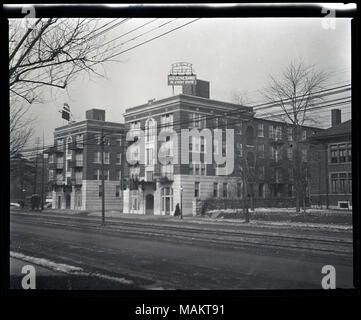 Horizontal, black and white photograph showing the two wings of the Harlan Court apartment building located at 5457 Delmar Boulevard. The apartment building has two four-story wings built of brick and stone. A sign that reads 'Harlan Court/An Electric Range in Every Suite' is on the roof of each wing. Metal balconies and a metal canopy on the front facade of the building can also be seen. The view was taken at an angle from across the street and shows the streetcar rails in the middle of the road. A horse pulling a covered cart can be seen in the distance on the left. Title: Harlan Court Apart Stock Photo