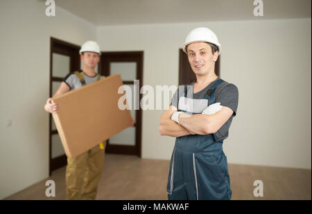 Theme of furniture delivery. Two loaders inside empty flat with box. Stock Photo