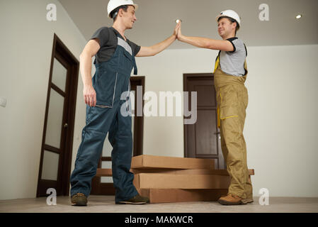 Two loaders finished with furniture delivery. Two workers made high five on big boxes background. Stock Photo