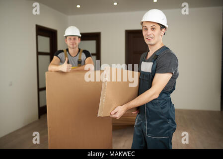 Furniture delivery theme. Two loaders move furniture in boxes into empty apartment. Stock Photo