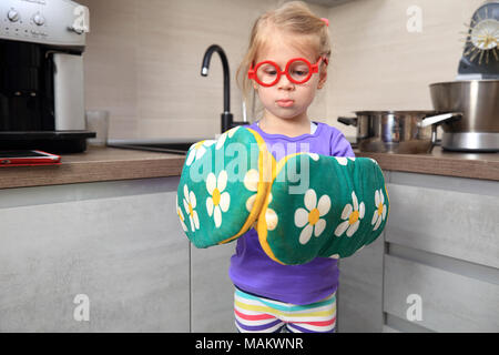 Kid with kitchen mittens. Funny little girl wearing big kitchen gloves. Stock Photo