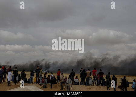 Palestinian protesters watch clouds of smoke as they rise from burnt tyres, to distract Israeli troops, during clashes along the borders between Israel and Gaza, east of Khan Yunis, southern Gaza Strip, 03 April 2018. Photo: Mohammed Talatene/dpa Stock Photo