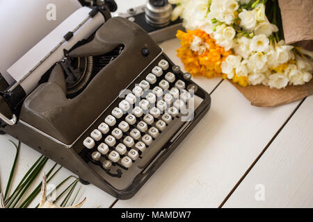 Freelance and writing concept. Retro typewriter on white wooden tabletop with flowers and vintage camera blurred. Stock Photo