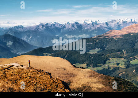 Young man hiker in bright jacket stands on cliff at mountains Dolomites and takes photography of valley, Italy, Seceda. Traveler enjoys landscape Stock Photo