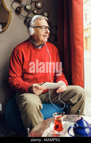 Portrait of happy senior man who is chatting on digital tablet in a cafe. Stock Photo