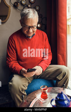 Senior man is sitting in cafe and typing message on mobile phone. Stock Photo