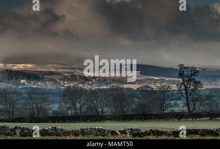 Teesdale landscape, a brief sunny interval highlights the rural conservation village of Barningham, with a fresh covering of snow on the moor behind Stock Photo