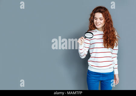 Positive smart woman looking into magnifying glass Stock Photo