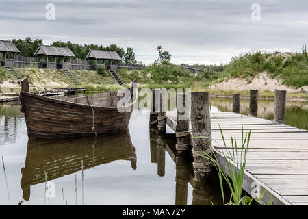 Tukums region, Latvia - July 8 2017: Medieval scenery near the lake with boat and wooden wall reflected in the water. Stock Photo