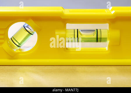Yellow spirit level on flat wooden surface. Close up horizontal image with space for text. Stock Photo
