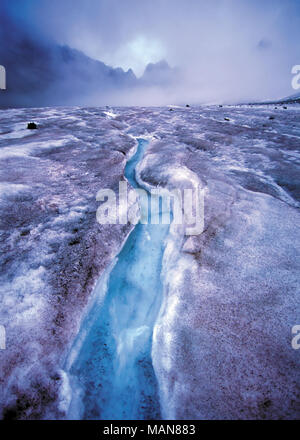 Bright blue creek in snow against foggy rocks, Arbuz glacier, Altai mountains, Russia Stock Photo