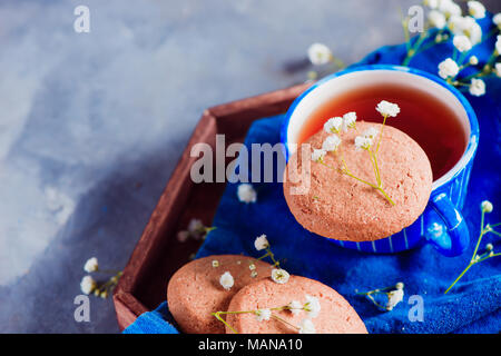 Morning scene with a small blue teacup and oatmeal cookies on a wooden tray with a blue linen napkin. High key snack concept with homemade pastry and  Stock Photo