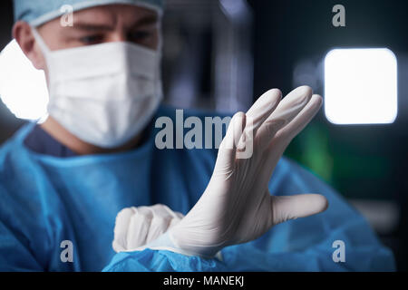 Male surgeon putting on latex gloves in preparation Stock Photo