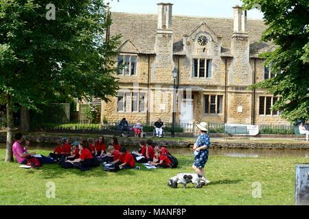 School children enjoying a lesson outdoors, the river windrush is in the background,  Bourton on the water, Gloucestershire, UK Stock Photo