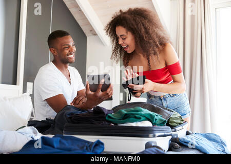 Couple Looking At Digital Tablet As They Pack For Vacation Stock Photo