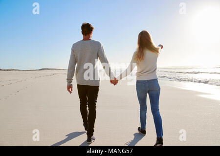 Rear View Of Loving Couple Walking Along Winter Beach Together Stock Photo