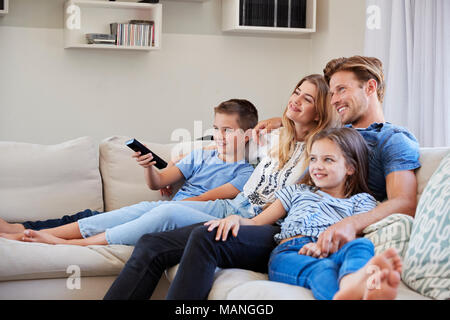 Family Sitting On Sofa At Home Watching TV Together Stock Photo
