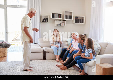 Multi Generation Family Sitting On Sofa At Home Playing Charades Stock Photo