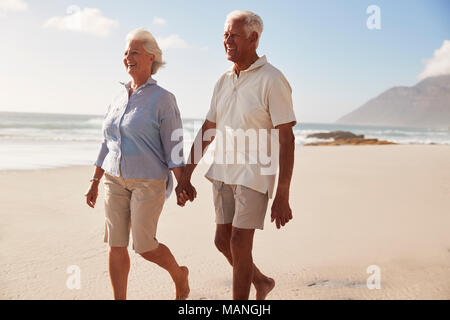 Senior Retired Couple Walking Along Beach Hand In Hand Together Stock Photo