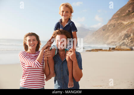 Portrait Of Parents Carrying Son On Shoulders On Beach Vacation