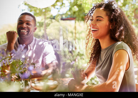 Young adult friends sitting at a table in a garden laughing Stock Photo