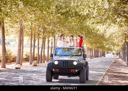 Girlfriends standing up in the back of an open top jeep Stock Photo