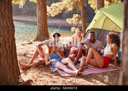 Friends on a camping trip relaxing on a blanket by a lake Stock Photo