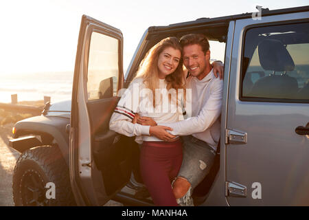 Young white couple on a road trip embracing by their car Stock Photo