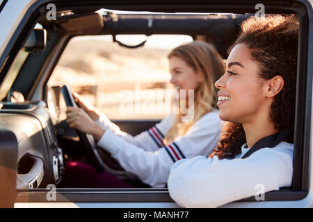 Two young female friends driving a car in the sun, side view Stock Photo