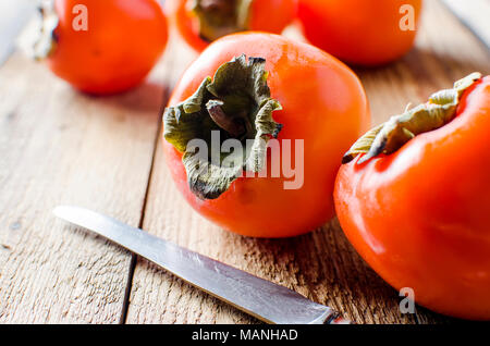 Sweet Ripe orange persimmons whole and chopped on an old wooden table in rustic style, selective focus . Copy space. Stock Photo