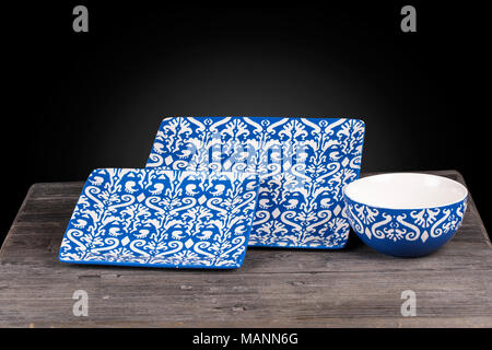 Close up of Traditional Floral Pattern Rectangle Plates and bowl tableware set  in white and turquoise blue color on a wooden table isolated on black  Stock Photo