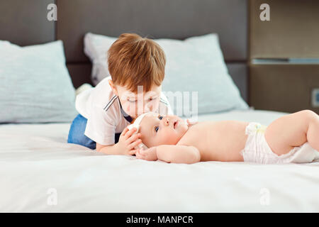 A little boy with his baby sister hugs and kisses on the bed. Stock Photo