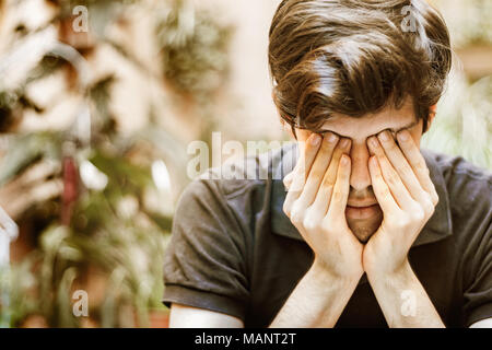 Young man sitting covering his eyes with his hands, sad and depressed concept. Stock Photo