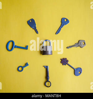 One lock and many different keys lie on a yellow background Stock Photo