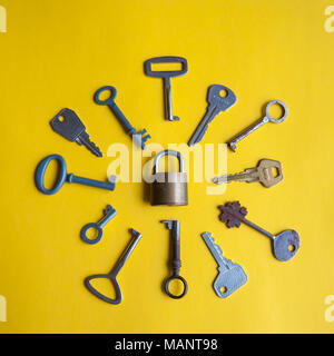 One lock and many different keys lie on a yellow background Stock Photo