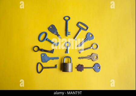 One lock and many different keys lie on a yellow background Stock Photo