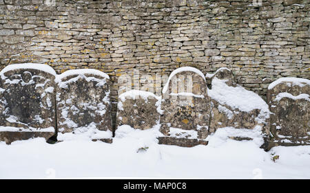 Row of gravestones against a dry stone wall in St. Mary's Churchyard in the winter snow. Bibury, Cotswolds, Gloucestershire, England Stock Photo