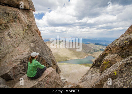 A female hike takes in the vista of surrounding mountains and alpine lakes from atop Mt. Evans in Colorado. Stock Photo