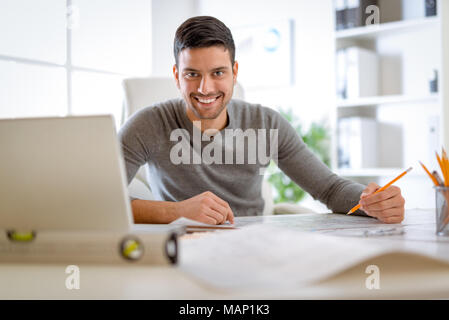 Young arabian male constructor analyzing blueprint at desk in office. Looking at camera. Stock Photo