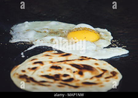 Frying the dough. Traditional Indian flatbread is fried with egg. Indian Breakfast. Street food in India. omelet, omelette, scrambled egg, fried egg Stock Photo