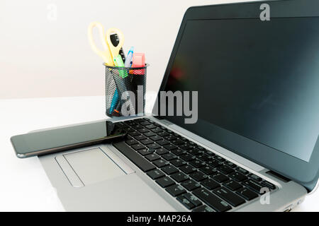 Office set up, Open laptop computer, smartphone and office supplies on white table. Clean and bright Stock Photo