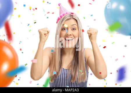 Young woman wearing a party hat gesturing happiness with confetti streamers and balloons flying around her isolated on white background Stock Photo