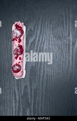 French traditional eclair, decorated with raspberry with cup of coffee on the dark wood table Stock Photo